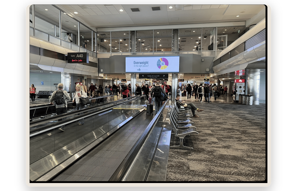 An airport concourse with a client's ad on the digital screen above the walkway